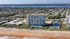 Een hoog hotel met zwembad, omgeven door een woongebied en een strand.