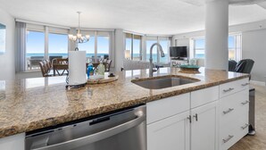 Een moderne keuken met granieten werkbladen, roestvrijstalen apparatuur en een groot raam met uitzicht op de oceaan.
