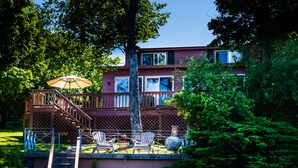 Ein zweistöckiges Haus mit einer Terrasse, Sitzgelegenheiten im Freien und einer Treppe, die zur Terrasse führt.