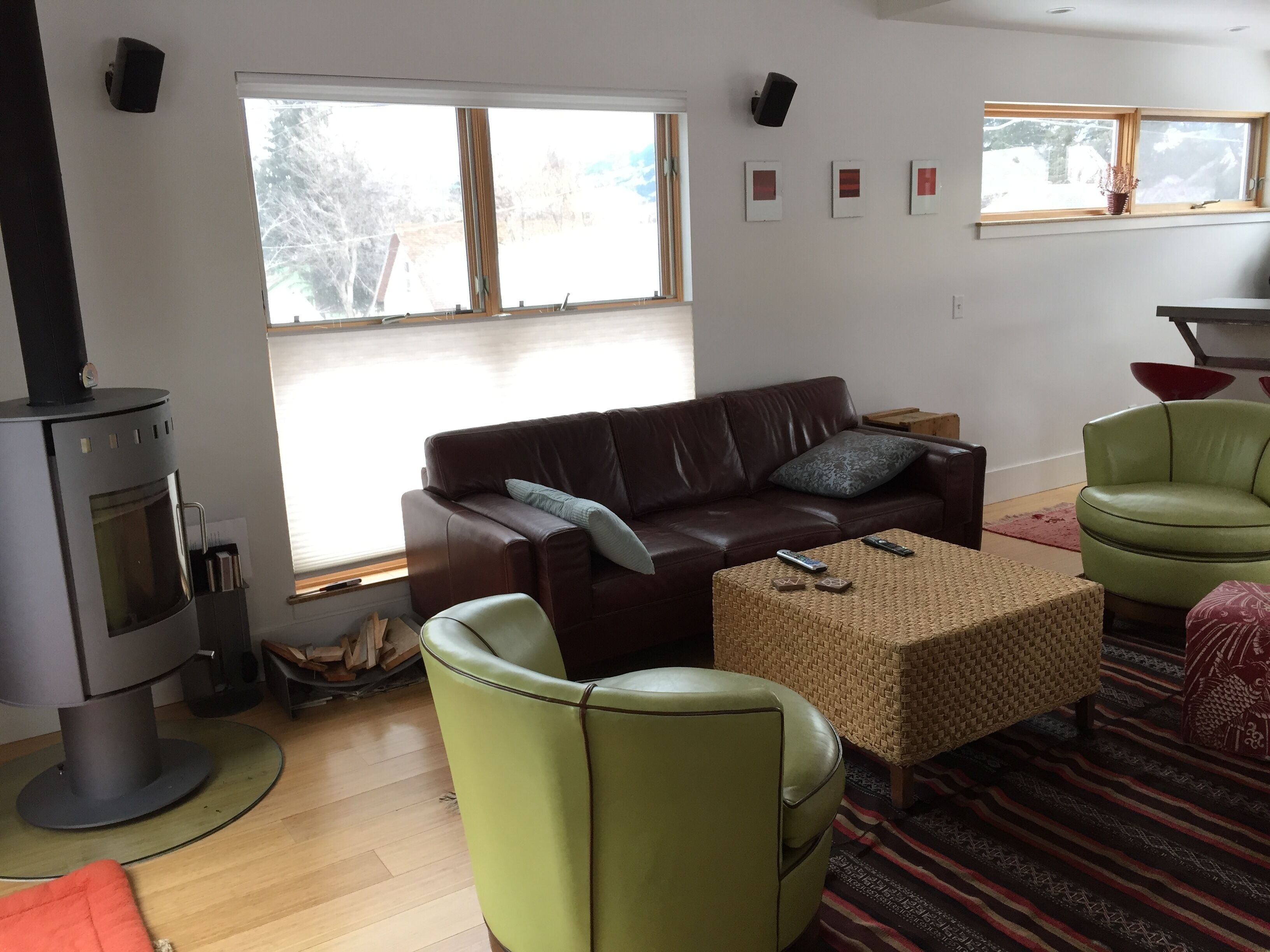 Un salón con sofá de cuero marrón, un sillón verde, un reposapiés tejido y una chimenea.