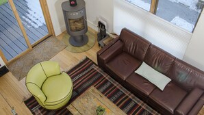 A living room with a brown leather sofa, a green armchair, a wooden coffee table with a plant, a fireplace, and a view of the outdoors through a window.