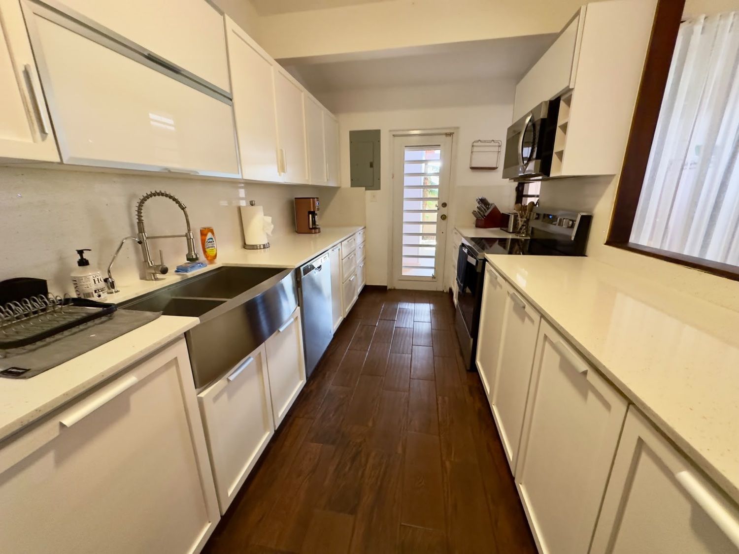 A kitchen with white cabinets, stainless steel appliances, and a wooden floor.