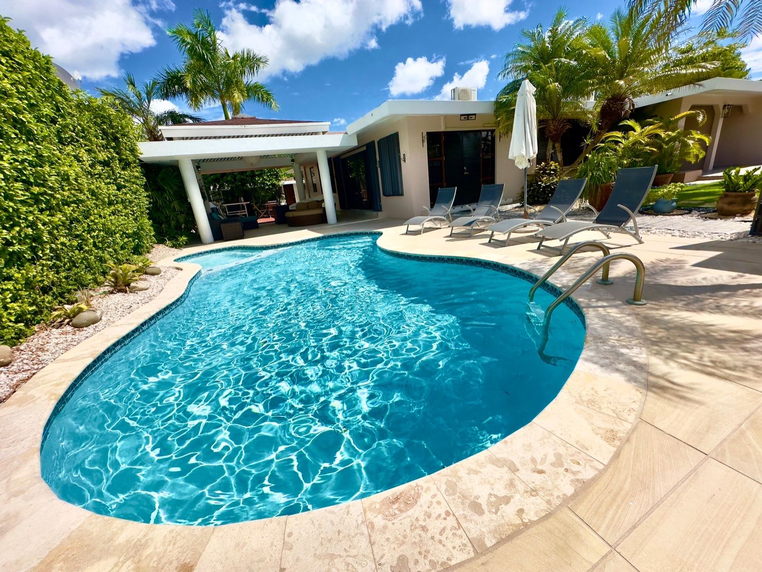 A swimming pool with a curved edge, surrounded by lounge chairs and a covered patio area.