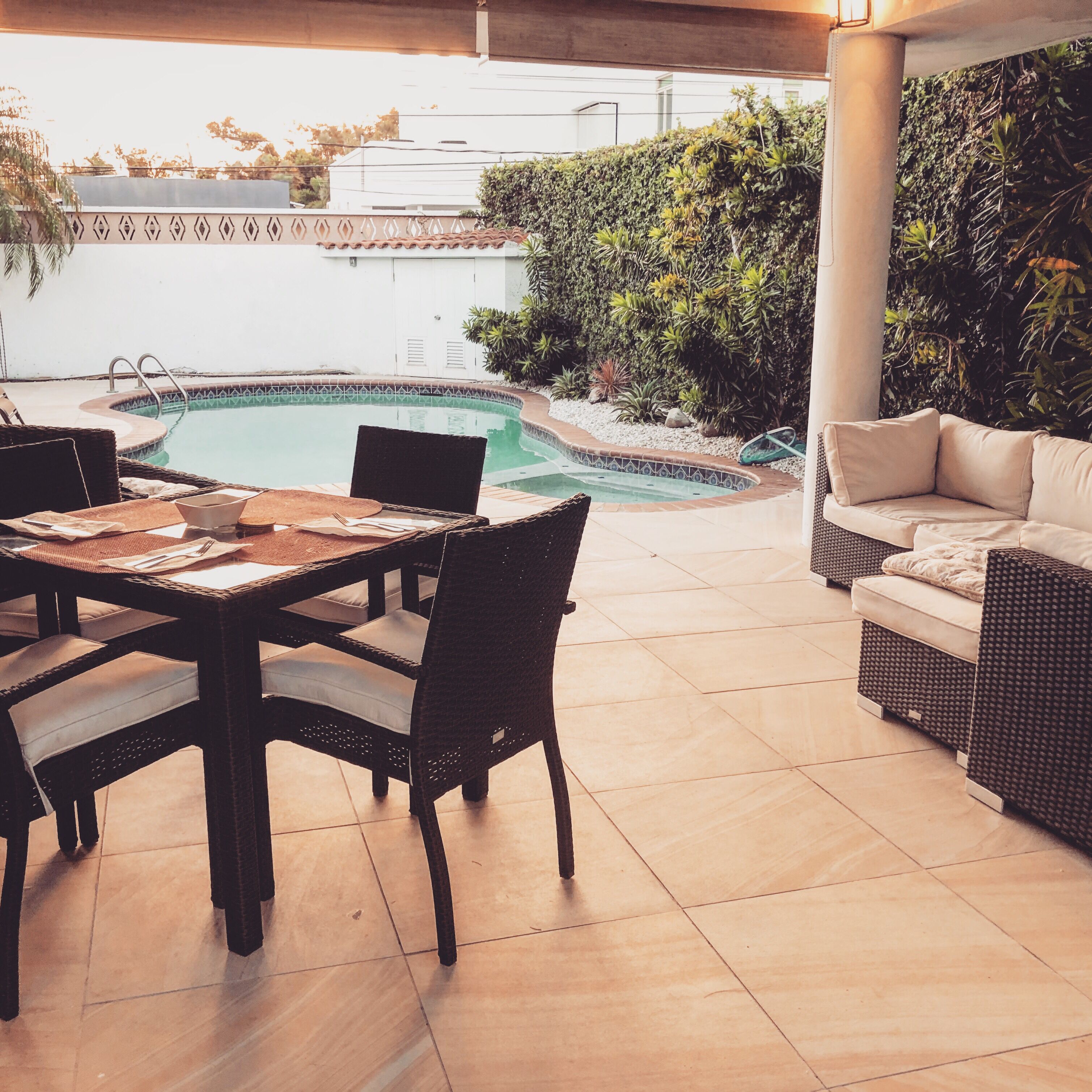 An outdoor patio with a pool, wicker furniture, and a view of a building in the background.