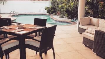An outdoor patio with a pool, wicker furniture, and a view of a building in the background.