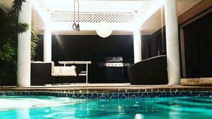 Ein Schwimmbad mit überdachtem Patio, Grill und Sitzgelegenheiten im Freien.