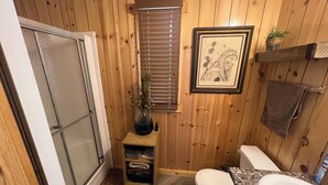 Un baño pequeño con paneles de madera, que incluye un inodoro, un lavamanos y una ventana con persianas.