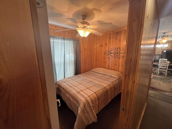 A bedroom with a bed, wooden walls, a ceiling fan, and a window with curtains.