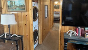 Un cuarto de lavandería con lavadora, lámpara, un cuadro enmarcado y televisor.