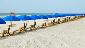 Una spiaggia con file di ombrelloni blu e sdraio di legno allineate sulla sabbia.