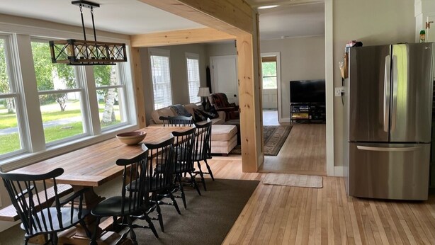 Una cocina amplia con una mesa y sillas de madera, un refrigerador de acero inoxidable y ventanas grandes que ofrecen vistas al exterior.