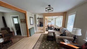 Un salón espacioso con piso de madera, un tapete grande, un conjunto de sofás y una zona de comedor con mesa y sillas.