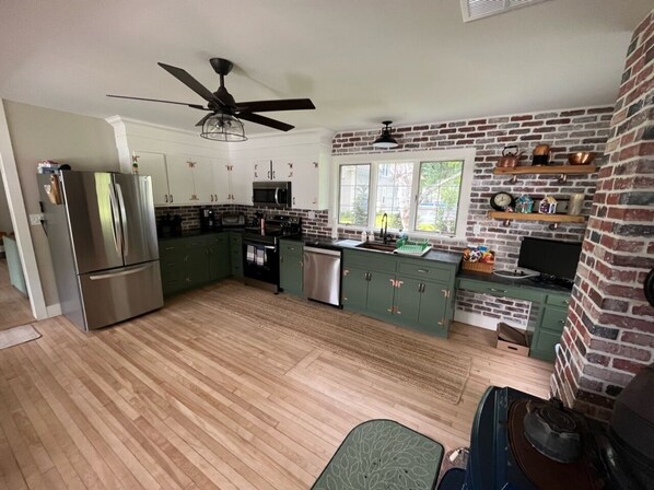 A modern kitchen with green cabinets, stainless steel appliances, and a brick accent wall.