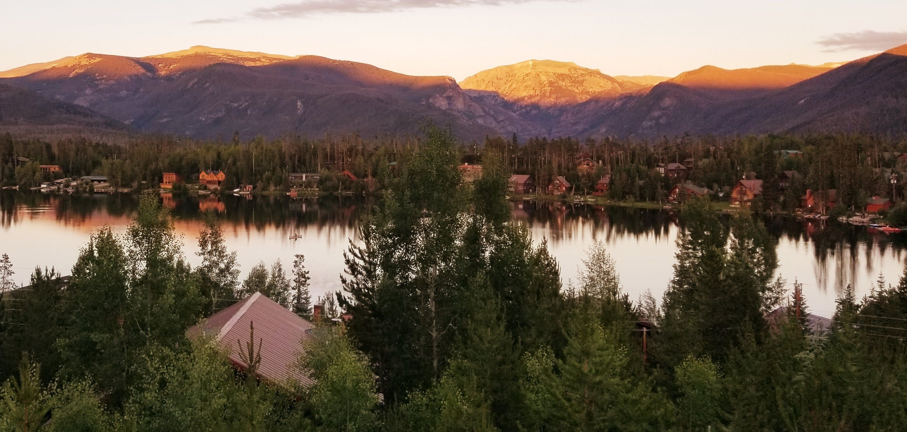 Un village au bord d’un lac, avec des maisons et une chaîne de montagnes en arrière-plan.