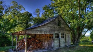 A rustic wooden cabin with a covered porch, a stack of firewood, and a large tree nearby. - Mountain Top Eureka Springs Cabin with Full Glass Front Best Views in Eureka (Eureka Springs)