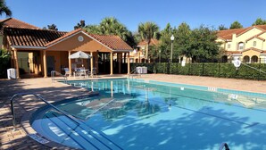 A swimming pool with a tiled deck, a covered seating area, and a fenced garden.