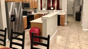 A modern kitchen with wooden cabinets, stainless steel appliances, a central island, and a red trash bin.