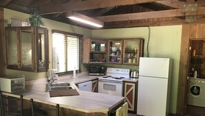 Een keuken met houten kasten, een centraal eiland met stoelen, een spoelbak, een fornuis, een magnetron en een wasmachine.
