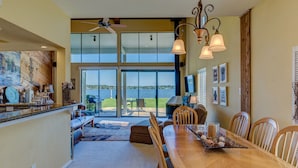 A spacious dining area with a large wooden table, surrounded by chairs, and a view of a lake through large windows. - WATERFRONT CONDO  WITH AMAZING VIEW OF SUNRISE, SUNSET AND EXPANSIVE OPEN WATERS (Montgomery)