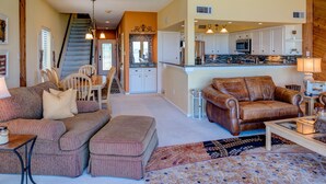 A spacious living room with a large sofa, a coffee table, and a patterned rug. There is a staircase leading to an upper level with a kitchen and dining area. - WATERFRONT CONDO  WITH AMAZING VIEW OF SUNRISE, SUNSET AND EXPANSIVE OPEN WATERS (Montgomery)