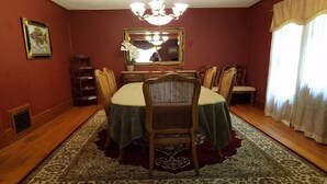 Ein Esszimmer mit einem runden Tisch, Stühlen, einer Chandelüster, einem Spiegel und einem Fenster mit Vorhängen.