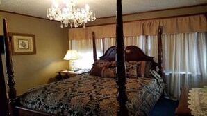 Ein Bett mit Baldachin, ausgestattet mit einer blumigen Tagesdecke, einer Kristallleuchtre, einem Nachttisch mit Lampe und einem gerahmten Bild an der Wand.
