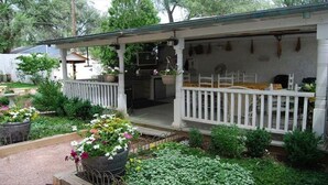 Eine überdachte Veranda mit weißer Geländer, ein kleiner Garten mit Topfpflanzen und ein sichtbarer Außenbereich mit Küche.