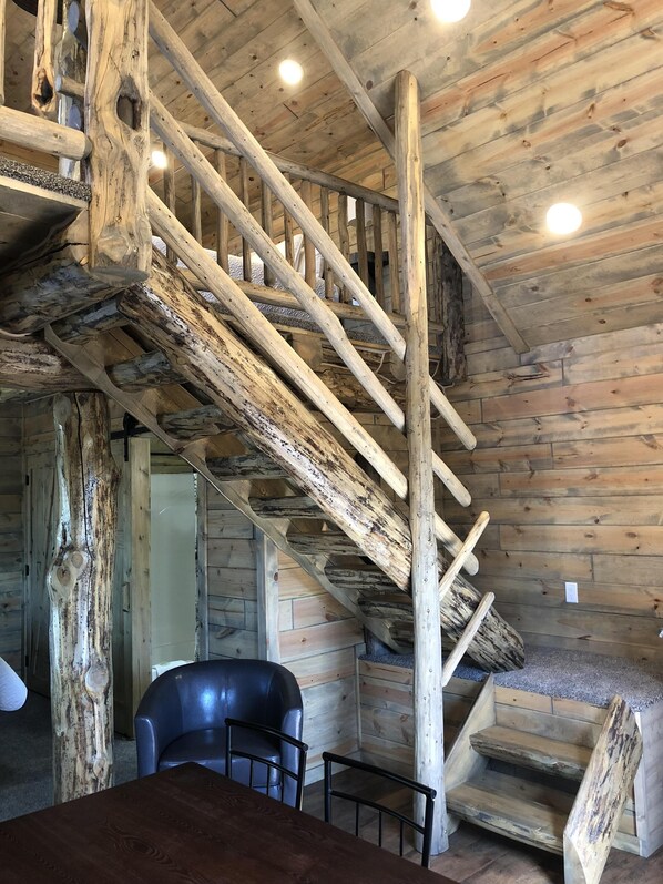 Una rústica escalera de madera con acabado natural, un sillón de cuero y una mesa en un interior de estilo cabaña.