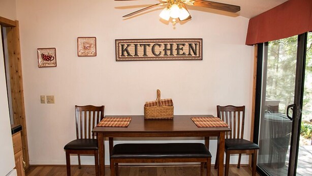 Uma cozinha com uma mesa de jantar, cadeiras, um ventilador de teto e uma placa na parede com a palavra 'KITCHEN'.