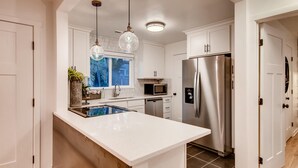 Una cocina moderna con armarios blancos, electrodomésticos de acero inoxidable, una isla grande, luces colgantes y vistas al exterior.