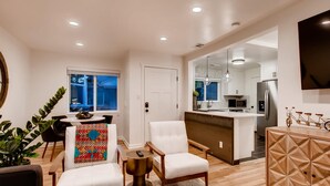 Una sala de estar moderna con comedor, una cocina con isla central, y vista al exterior.