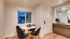Cocina compacta con comedor, que presenta una puerta blanca, un ventanal con vista al exterior y una lámpara moderna.