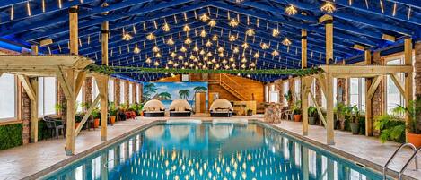 An indoor swimming pool with a ceiling adorned with hanging lights, wooden beams, and a tropical mural in the background.