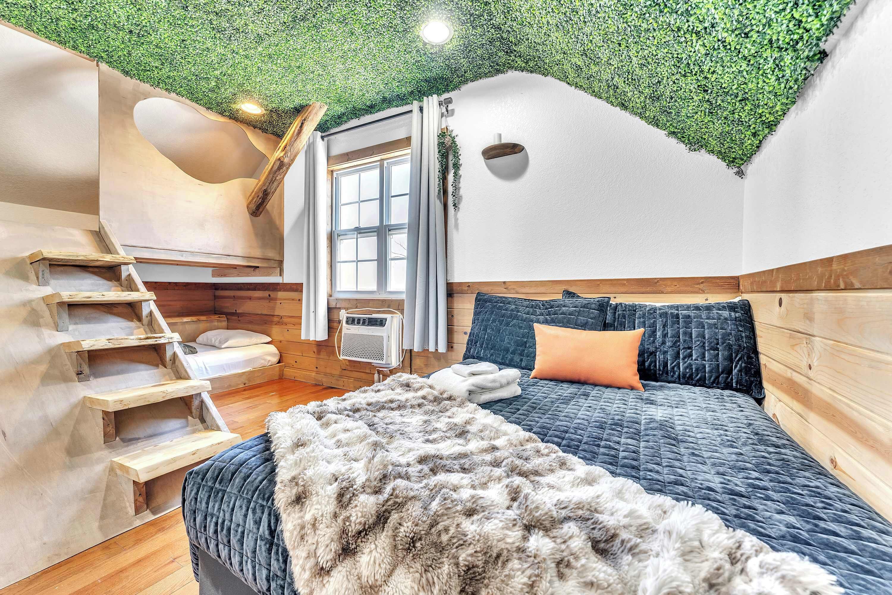 A bedroom with a unique green ceiling, wooden walls, a bed with blue bedding, and a staircase.
