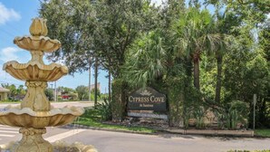 Una fuente, un cartel que dice Cypress Cove at Suntree y abundante vegetación.