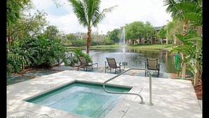 Zona de piscina con jacuzzi, sillones de descanso y vista a un lago con una fuente.