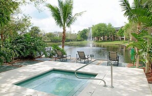 Zona de piscina con jacuzzi, sillones de descanso y vista a un lago con una fuente.