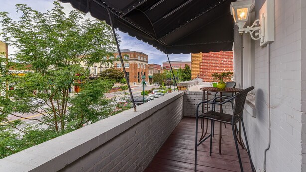 Un balcon donnant sur une rue de la ville, une table avec des chaises et une plante en pot.