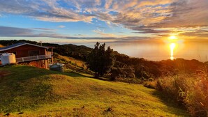 A house with a balcony overlooking a grassy hill and a sunset over a body of water. - Over the Horizon near Savusavu Market (Savusavu)