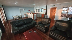 A living room with a sofa, armchairs, and a coffee table. There is a dining area with a table and chairs, and a kitchen in the background. - Over the Horizon near Savusavu Market (Savusavu)