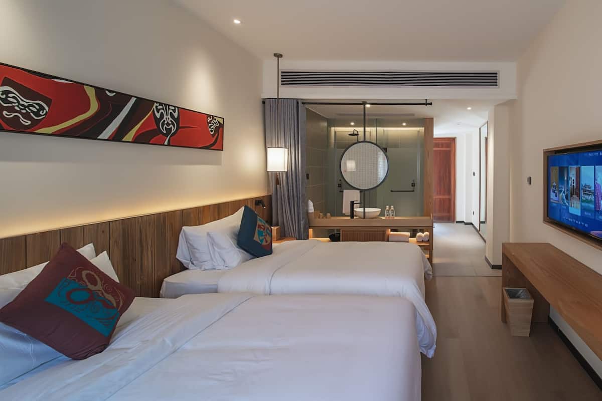 A hotel room with two beds, a large mirror, a TV, and a wooden headboard.