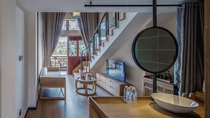 A modern living room with a wooden floor, a round mirror, a wooden coffee table, a TV, and a view of a balcony. - Grand House Chongqing (Chongqing)