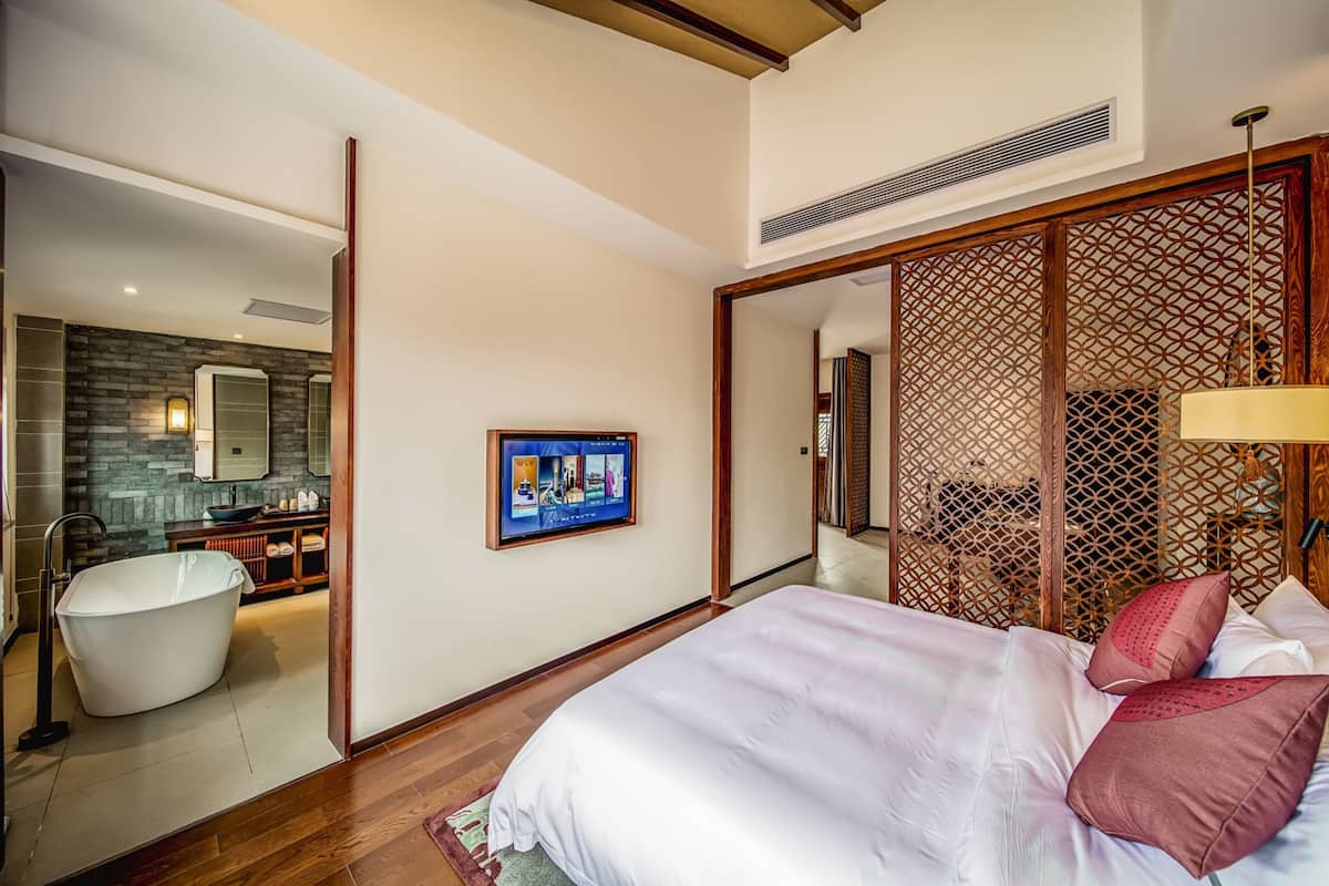 A modern hotel room with a large bed, a bathtub, a TV, and a wooden partition.