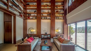 A spacious living area with high wooden bookshelves, two sofas, a coffee table, and a large window offering a view of the outdoors. - Grand House Chongqing (Chongqing)