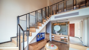 A modern interior with a wooden staircase, a round table with a bowl of fruit, and a television on a wooden cabinet. - Grand House Chongqing (Chongqing)