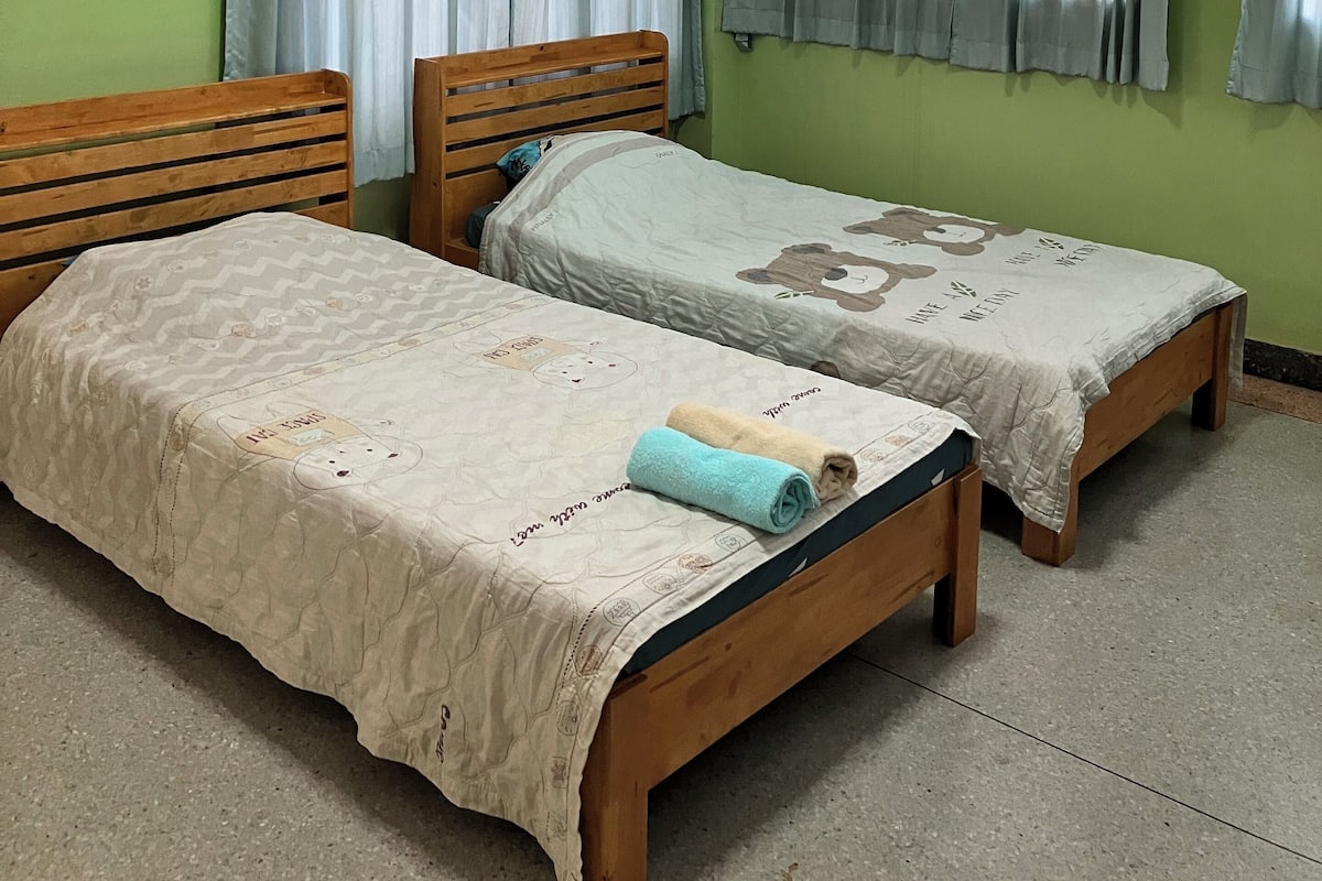 A room with two wooden beds, a ceiling fan, and light-colored walls.
