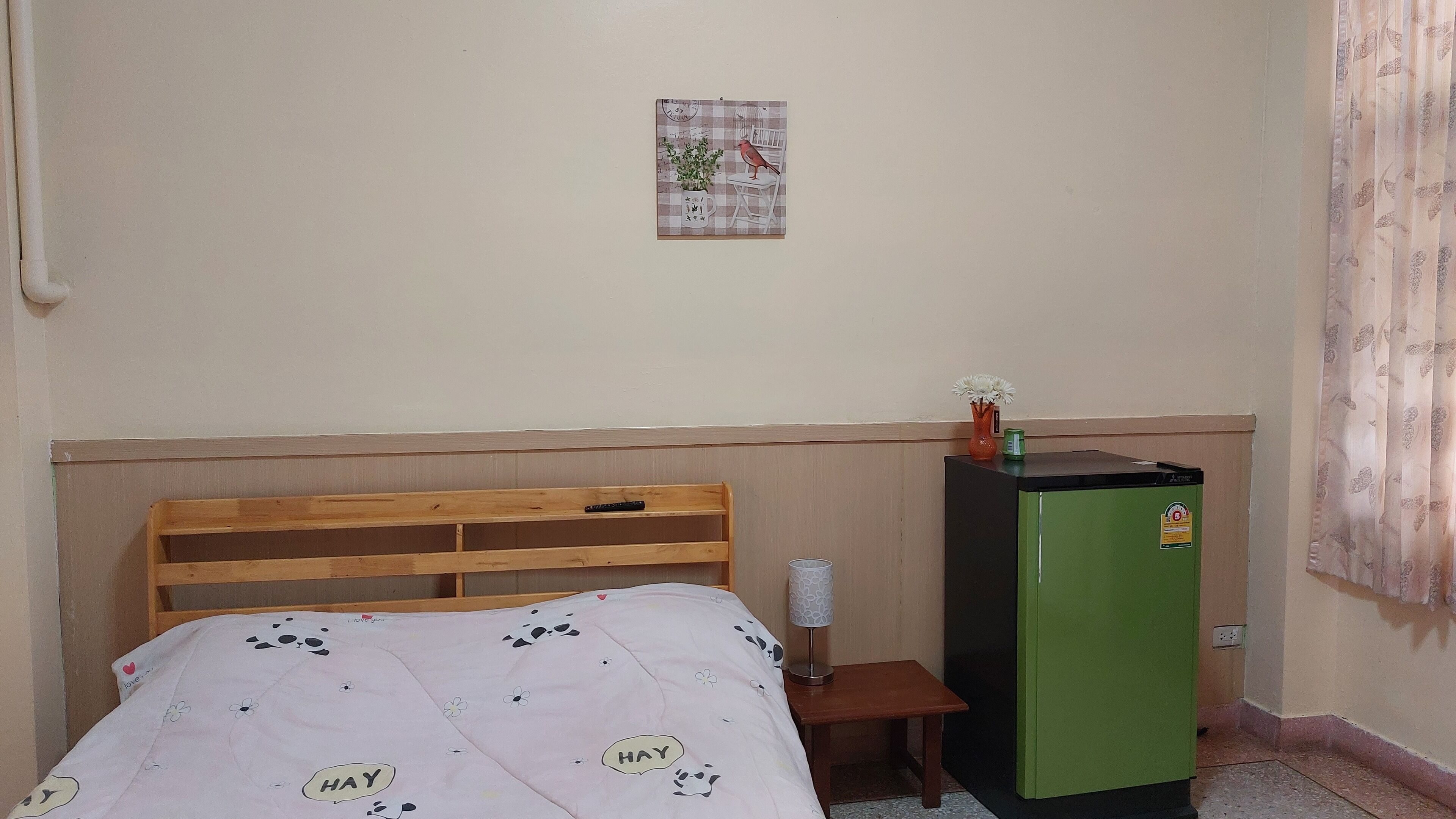 A bedroom with a wooden bed, a small bedside table, a green refrigerator, and a wall-mounted picture.