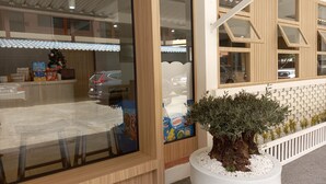 A modern building with a large glass window, a wooden facade, and a potted plant in the foreground. - Sataya Apartment (Maha Sarakham)
