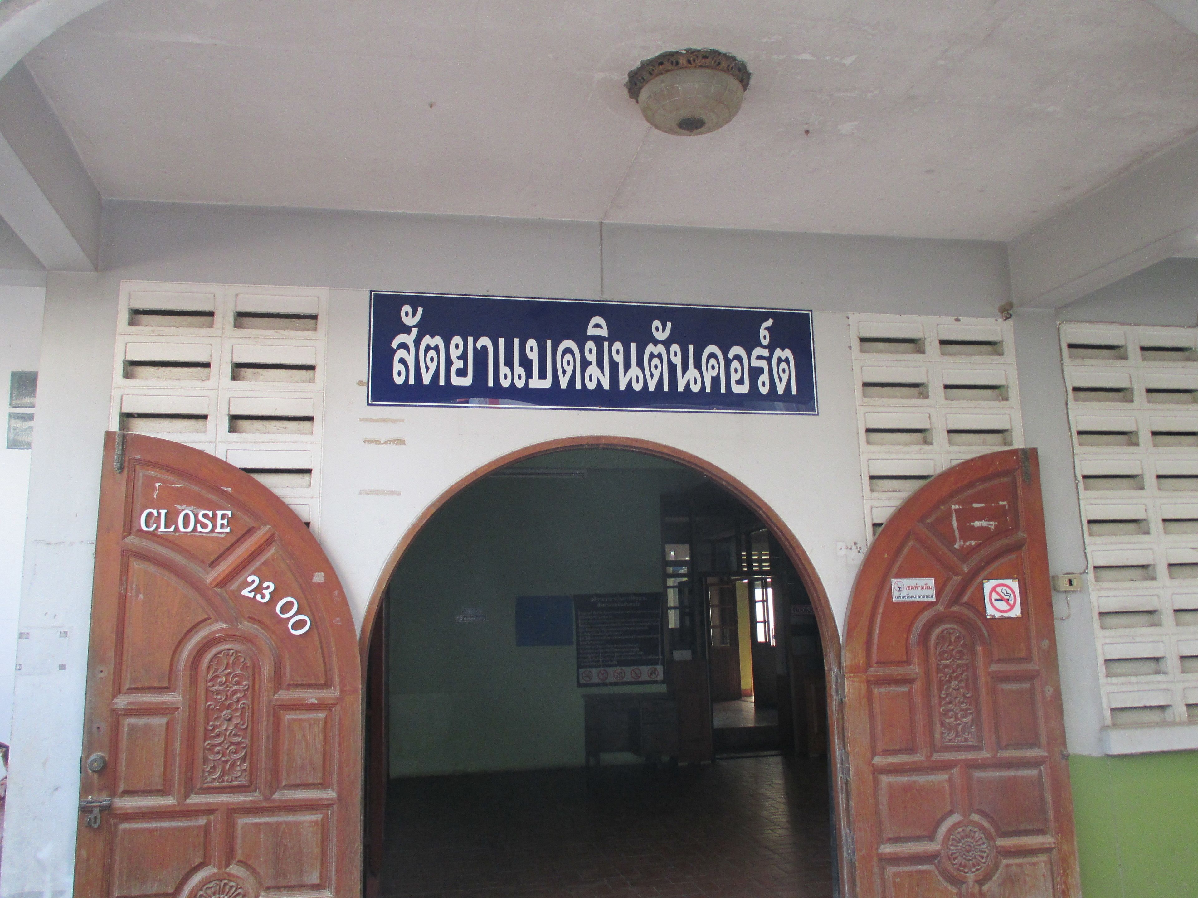 A building entrance with a sign in a foreign language, two wooden doors with "CLOSE" and "23:00" signs, and a ceiling light fixture.
