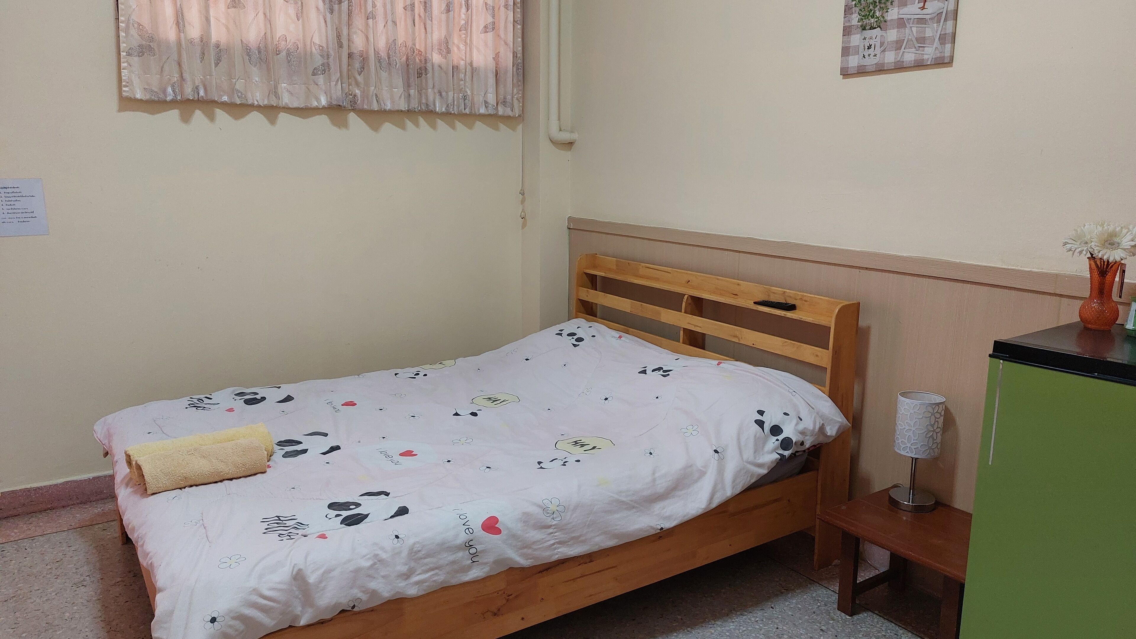 A single bed with a wooden headboard, a bedside table with a vase, and a wall-mounted calendar.